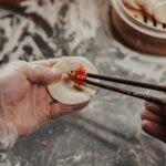 Dłonie w rękawiczkach nadziewające pierogi w kuchni