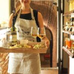 Kelnerka w retro fartuchu podaje wino i przystawki w rustykalnym wnętrzu