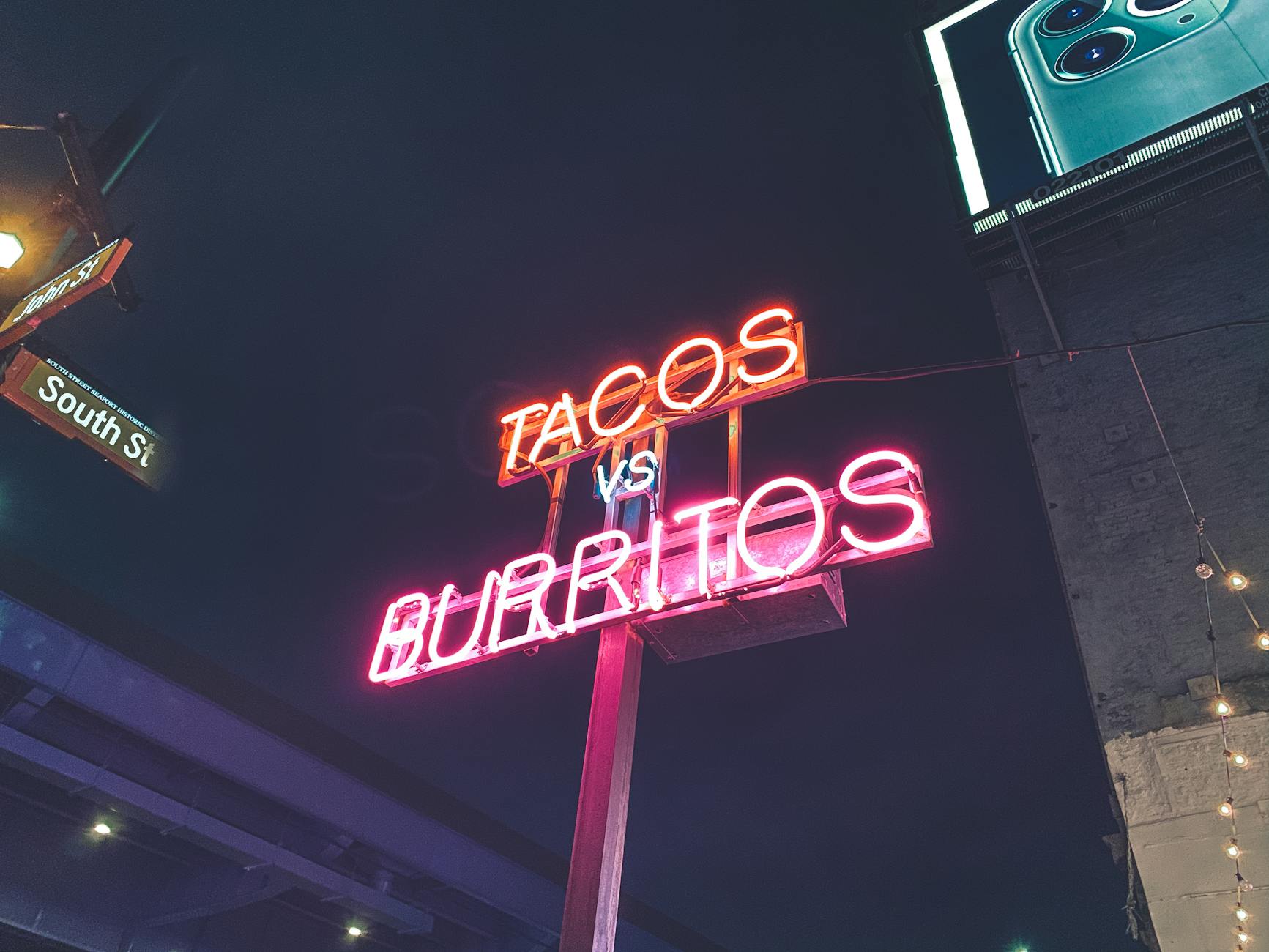 Neonowy napis Tacos vs Burritos na ulicy nocą Neonowy napis Tacos vs Burritos na ulicy nocą