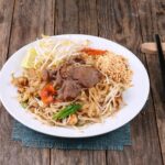 Pad thai z wołowiną, orzeszkami i warzywami na drewnianym stole