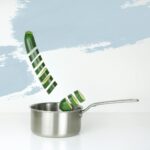 Plasterki cukinii spadające do patelni na jasnym tle